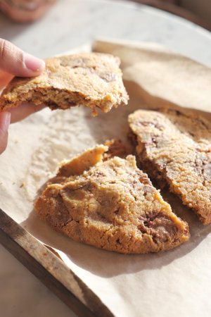 Deliciously Freshly Baked Cookies Placed on Parchment Paper with a Hand Holding One Pieceの写真素材