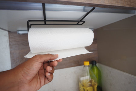 A hand holds a paper towel roll in a stylish kitchen, highlighting its practical use and beautyの写真素材
