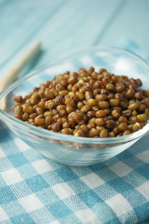 A beautiful glass bowl filled with brown sprouted mung beans sitting on a blue checkered tableclothの写真素材