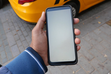 A person is holding a smartphone while standing in a vibrant urban environment during the dayの写真素材