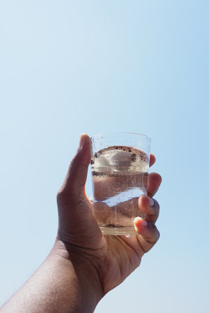 holding dirty glass of water against blue skyの写真素材