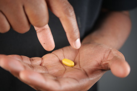 A person is holding a yellow pill delicately with their fingers while pointing at it,の写真素材