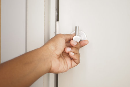 A hand is turning a door knob on a beautifully painted white door to gain entry inside