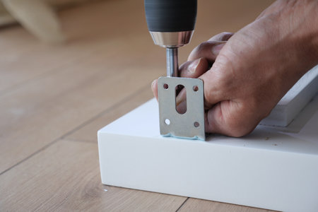 A person is using a power drill effectively to secure a metal bracket onto a clean white surfaceの写真素材