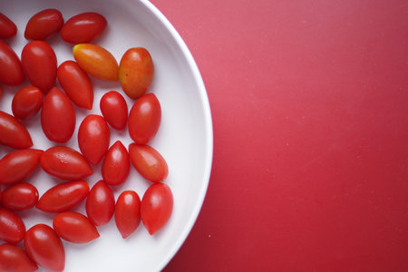 Assorted Cherry Tomatoes arranged on a white plate, with a vibrant red backgroundの写真素材