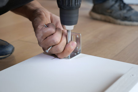 A person is using a power drill effectively to secure a metal bracket onto a clean white surfaceの写真素材