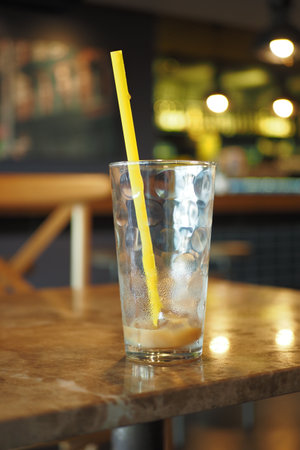 An Empty Glass Featuring a Yellow Straw is Placed on a Rustic Table Inside the Cafeの写真素材