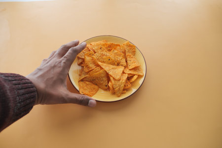 A Hand Gracefully Reaching for Some Crunchy Tortilla Chips That Are Present on a Plateの写真素材