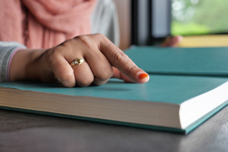 A hand points at an open book on a table, evoking calm and concentration in soft daylightの写真素材
