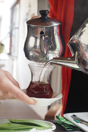 Pouring aromatic tea from a silver teapot into a clear glass cup, creating a delightful drinkの写真素材