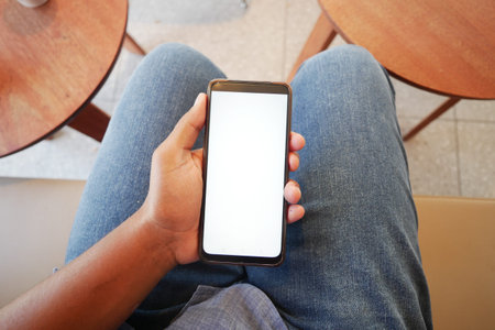 Individual comfortably holding a smartphone in a casual and relaxed setting during the daytime,