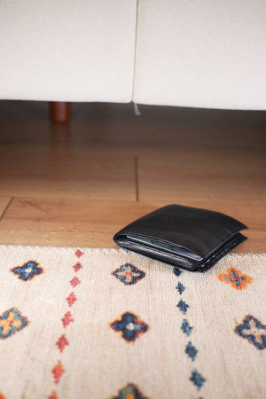 A sleek black wallet is resting on a cozy home rug positioned under the stylish sofa nearbyの写真素材