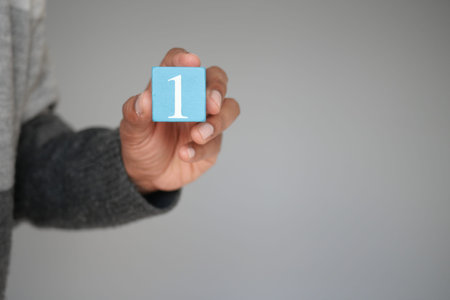 A hand is holding a blue block that has the number one inscribed on it against a neutral background