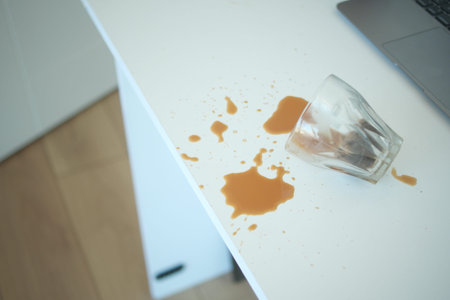 A drink was accidentally spilled on a desk with a laptop and glasses, creating a mess