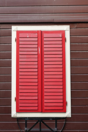 The vibrant and striking red shutters meticulously placed on a rustic wooden wallの写真素材