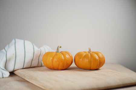 Two Fresh Pumpkins Beautifully Displayed on a Wooden Cutting Boardの写真素材