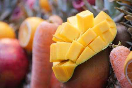 A colorful display featuring a variety of mangoes, apples, carrots, and other produce.の写真素材