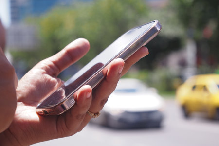 A person holding a smartphone on a busy urban street filled with trafficの写真素材