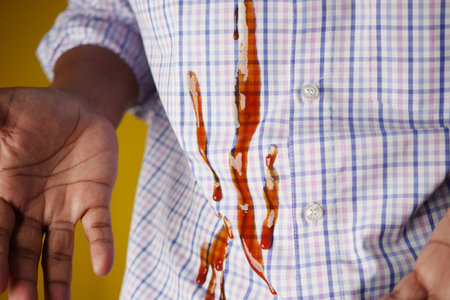 A yellow shirt was stained by spilled ketchup, requiring cleaning to remove the blot