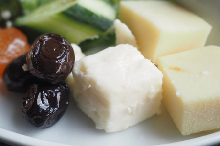 A beautifully arranged assortment of cheeses and fresh vegetables on a plateの写真素材