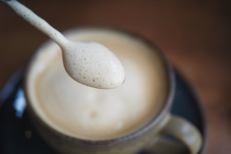 A closeup view showcasing a creamy coffee with beautiful swirls and a spoon resting in a white cupの写真素材