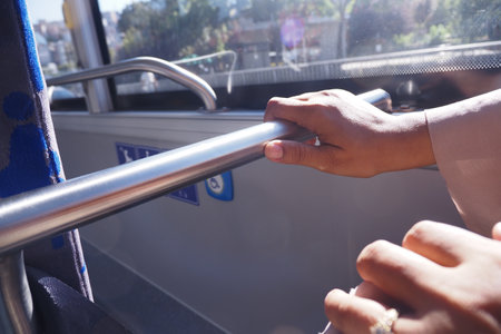 Close-up of Hands Holding Bus Rail in Sunny Public Transportの写真素材