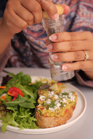 A person is joyfully adding a sprinkle of salt to a colorful, vibrant salad and crunchy toast dish,の写真素材