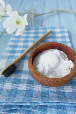 A wooden bowl of baking soda, a bamboo toothbrush, and a glass jar on a fabricの写真素材