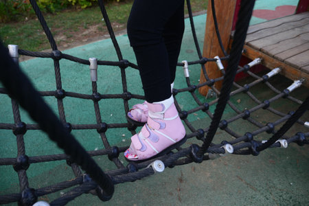 A little girl in orthosis shoes crosses a wooden bridge Child cerebral palsy disability.の写真素材