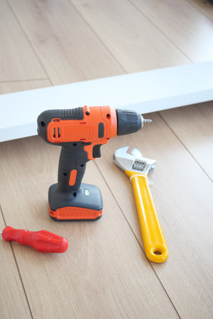 An electric drill is on the floor, along with a wrench and screwdriver.の写真素材
