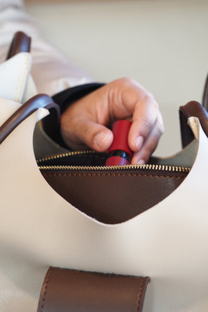 Woman hand is gracefully holding a lip gloss positioned above a purseの写真素材