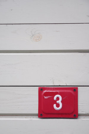 The vibrant Red Number 3 stands out against the White Wooden Wall surfaceの写真素材