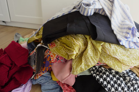 A Chaotic and Messy Pile of Various Colorful Clothes Scattered on a WellWorn Wooden Floor Surfaceの写真素材