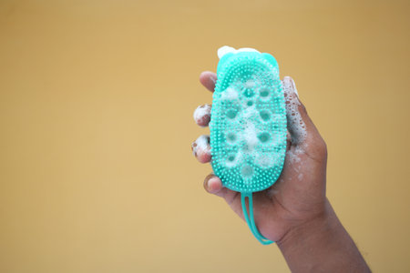 A hand is holding a green soap scrubber that is covered in foamの写真素材