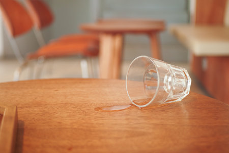 A glass has been spilled on a wooden table inside a modern cafe environmentの写真素材
