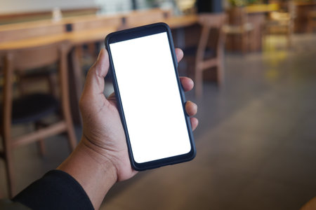 A hand is holding a smartphone while seated in a modern cafe environmentの写真素材