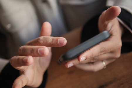 A detailed closeup view of hands utilizing a smartphone on a wooden tableの写真素材