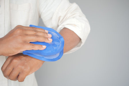 Person Applying Blue Ice Pack to Their Arm for Pain Relief or Injuryの写真素材