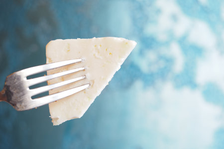 Delicious Triangle of Cheese on a Fork Against a Blue Backgroundの写真素材