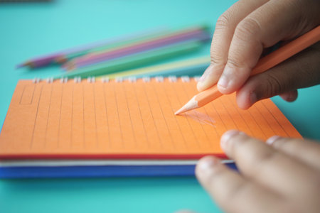 A Childs Hand is Holding a Brightly Colored Pencil on a Notepad for Drawingの写真素材