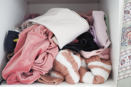 Messy closet with piled clothes and colorful accessories, displaying chaos and disorder in storageの写真素材