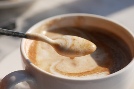A closeup view showcasing a creamy coffee with beautiful swirls and a spoon resting in a white cupの写真素材