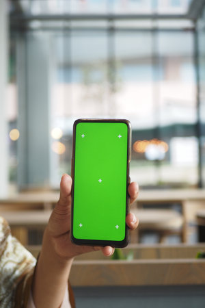 A person with a smartphone on a green screen sits in a cafeの写真素材