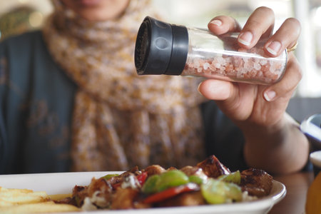 A person is skillfully seasoning a meal with pink salt inside a restaurantの写真素材