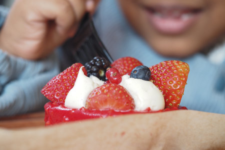 A child enjoys a colorful fruit tart topped with strawberries and blackberriesの写真素材
