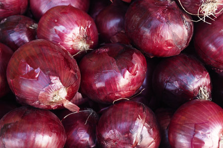 Fresh red onions piled in a vibrant bustling market settingの写真素材