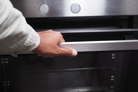 A person is using their hand to open a modern oven, engaging in culinary activities at homeの写真素材