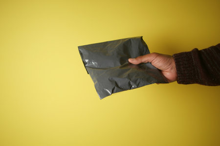 An Individual Holding a Small Package Against a Bright Yellow Backgroundの写真素材