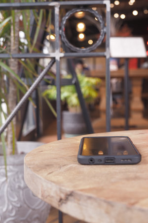 Mobile phone rests on wooden table in lively cafe environment with blurred backgroundの写真素材