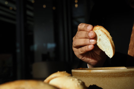 Hand dipping bread slice into a bowl filled with sauce at cafe